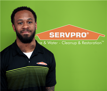 A man in a SERVPRO shirt smiling at the camera with a green backdrop and a SERVPRO logo